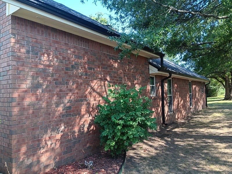 New dark gutters and downspouts along the side of a brick home in Bartlesville, Oklahoma