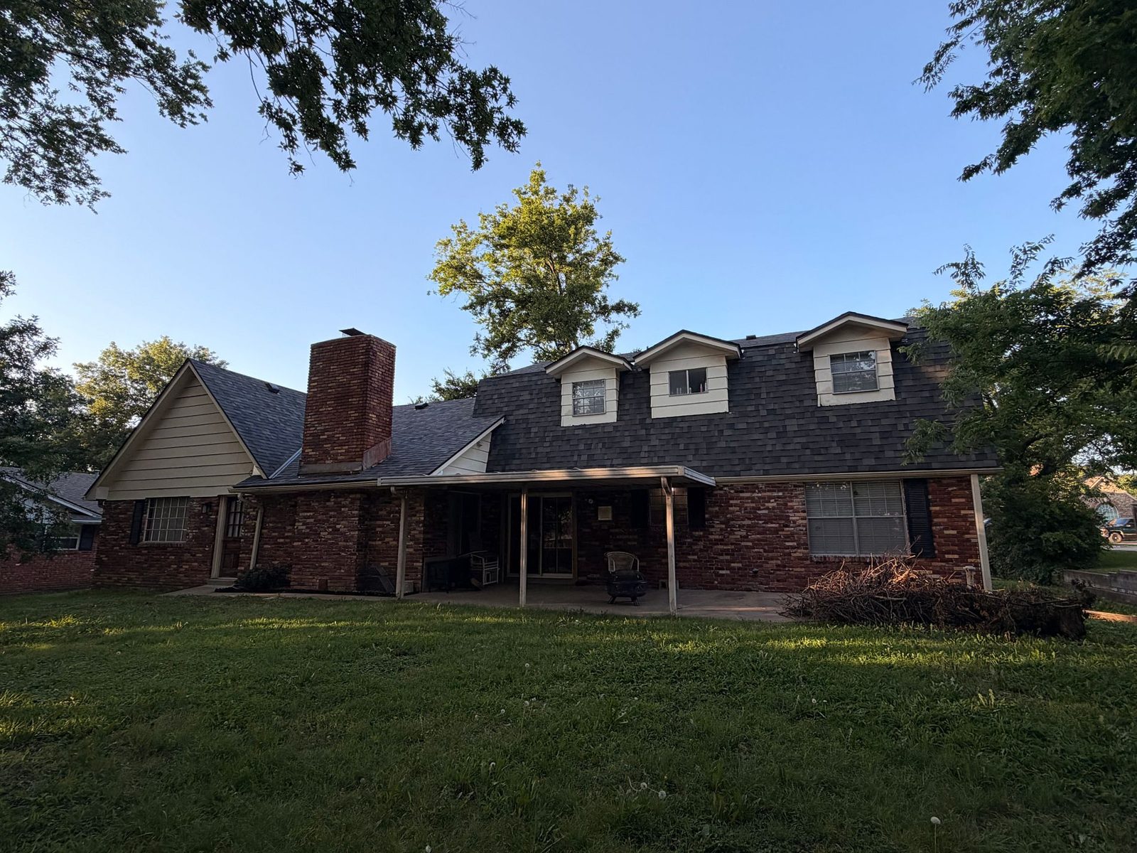 Rear view of a Bartlesville, Oklahoma home with new Malarkey Highlander AR Storm Grey shingles, dormers and a brick chimney